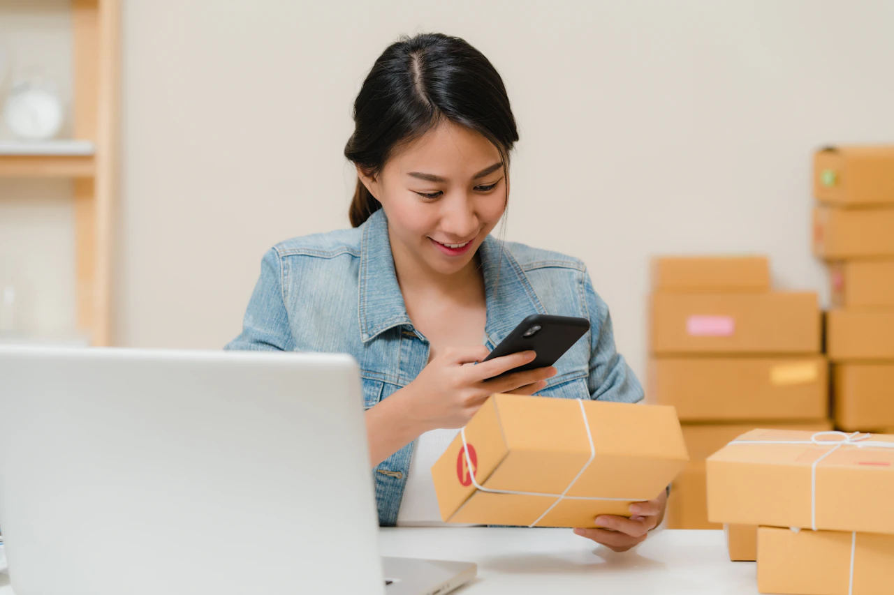 Responsable de una tienda online atendiendo mensajes desde el móvil junto a los pedidos preparados